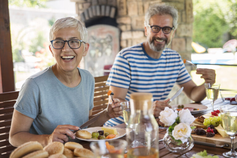 Two seniors, a female with short hair and a male in a striped shirt, having summer lunch.